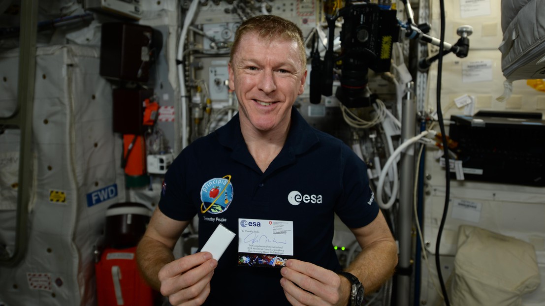 L'astronaute Time Peake (UK), tenant un des chocolats et la carte offerts par la Suisse. (c)ESA