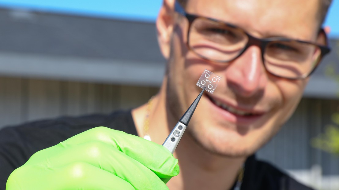 Matthieu Rüegg tenant au bout d'une pince quatre micro-résonateurs© 2019 EPFL / Murielle Gerber